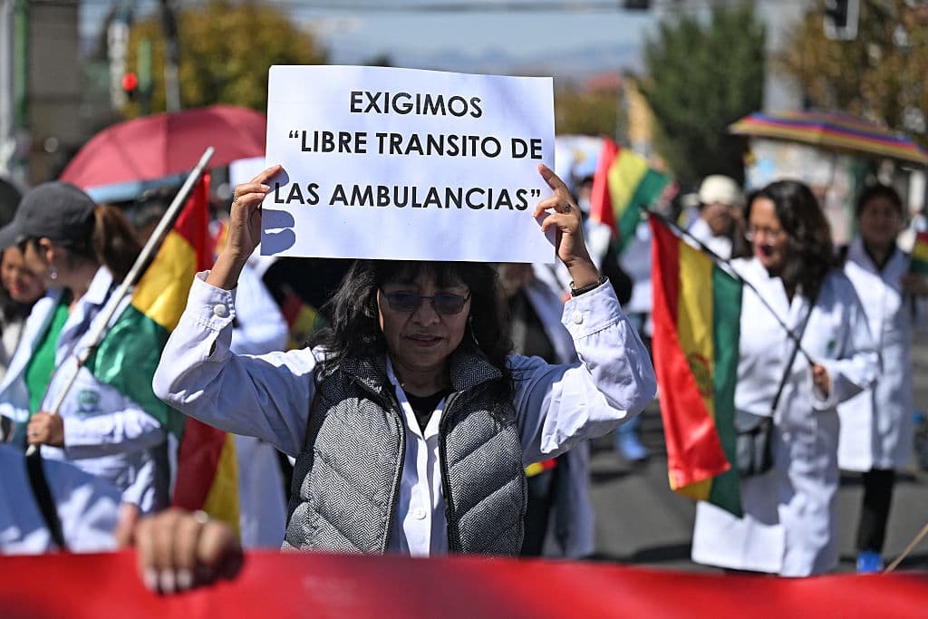<em>Una trabajadora de la salud alza un cartel que dice "Exigimos acceso sin obstáculos para las ambulancias" denunciando la escasez de alimentos, medicamentos y oxígeno que afecta la atención a pacientes, en La Paz, Bolivia, durante una protesta contra los bloqueos de carreteras y acceso a la ciudad de manifestantes que se oponen al presidente boliviano Rodrigo Paz, el 28 de mayo de 2026. (Foto de Marvin RECINOS / AFP vía Getty Images)</em>