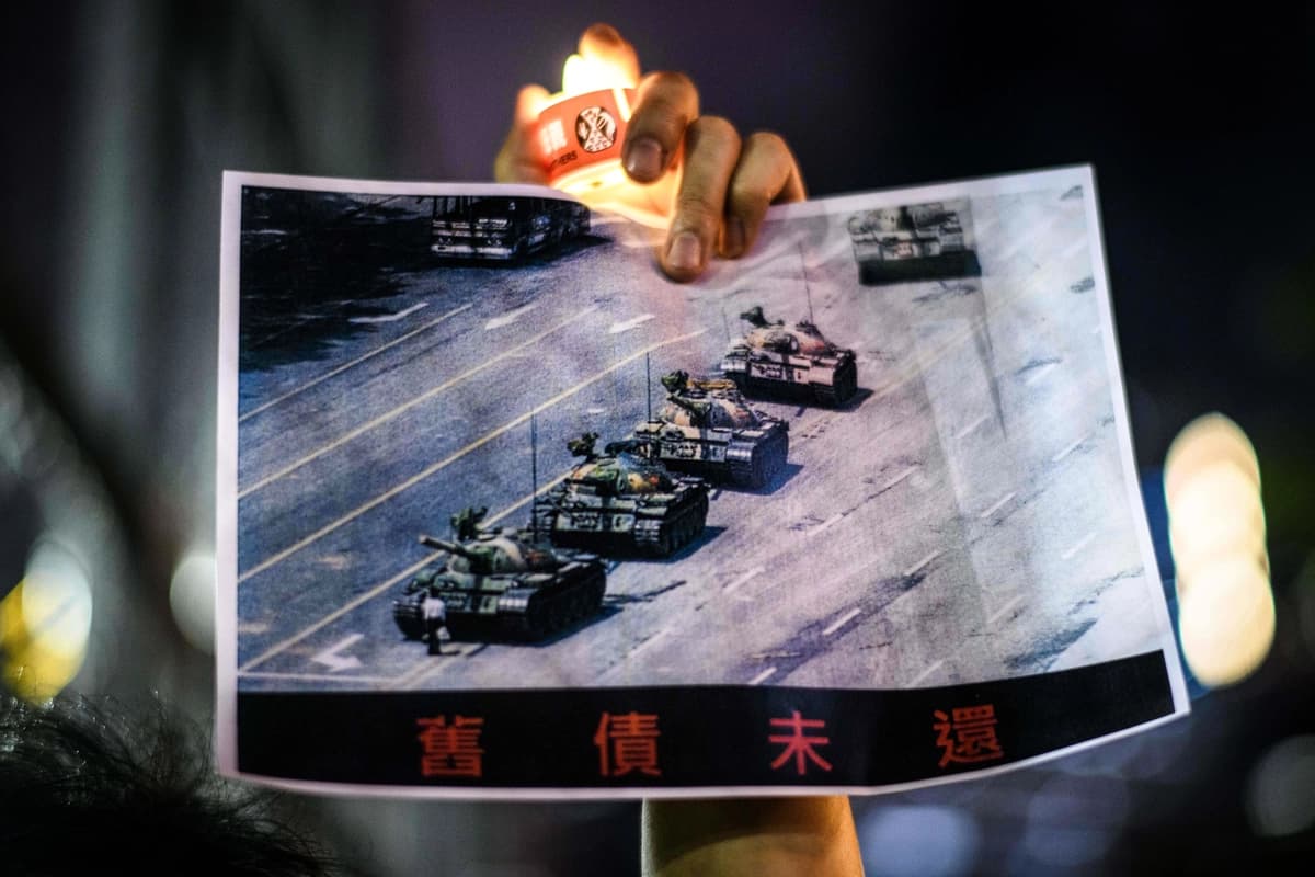 Un hombre sostiene un cartel del famoso "Hombre del Tanque" frente a los tanques militares chinos en la Plaza de Tiananmen el 5 de junio de 1989, durante una vigilia con velas en el Parque Victoria de Hong Kong el 4 de junio de 2020. (Anthony/AFP vía Getty Images)