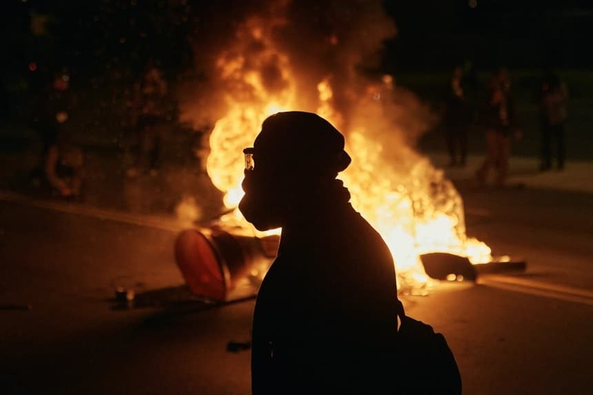 Un hombre con equipo de protección camina frente a una barricada en llamas frente al centro de detención Delaney Hall durante una protesta contra el traslado de detenidos y las políticas federales de inmigración en Newark, Nueva Jersey, el 30 de mayo de 2026. (Andrés Kudacki/AP Photo)

