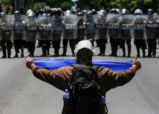 <em>Un manifestante muestra una bandera nicaragüense a un grupo de policías antidisturbios que bloquean una calle durante una protesta contra el gobierno del presidente nicaragüense Daniel Ortega en Managua. Imagen de archivo. Foto de INTI OCON/AFP vía Getty Images</em>
