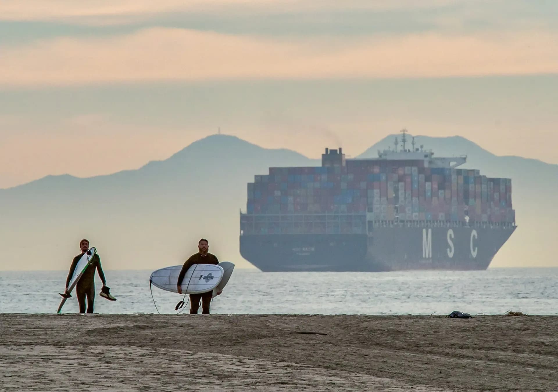 Los surfistas salen del agua mientras un buque cargado de contenedores se cierne frente a la costa de Seal Beach, California, el 12 de enero de 2021. La mayoría de los productos manufacturados que se comercializan a nivel internacional se transportan en estas "cajas", que se han convertido en las unidades del comercio mundial. (John Fredricks/The Epoch Times)