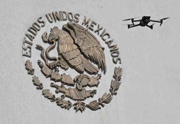 <em>Un dron sobrevuela el emblema nacional de México durante una demostración del batallón especial antidrones del Ejército mexicano en el Campamento Militar Número 1 de Naucalpan, Estado de México, el 17 de febrero de 2026, como parte de los preparativos para proteger las sedes del Mundial de 2026. (Alfredo ESTRELLA / AFP vía Getty Images)</em>