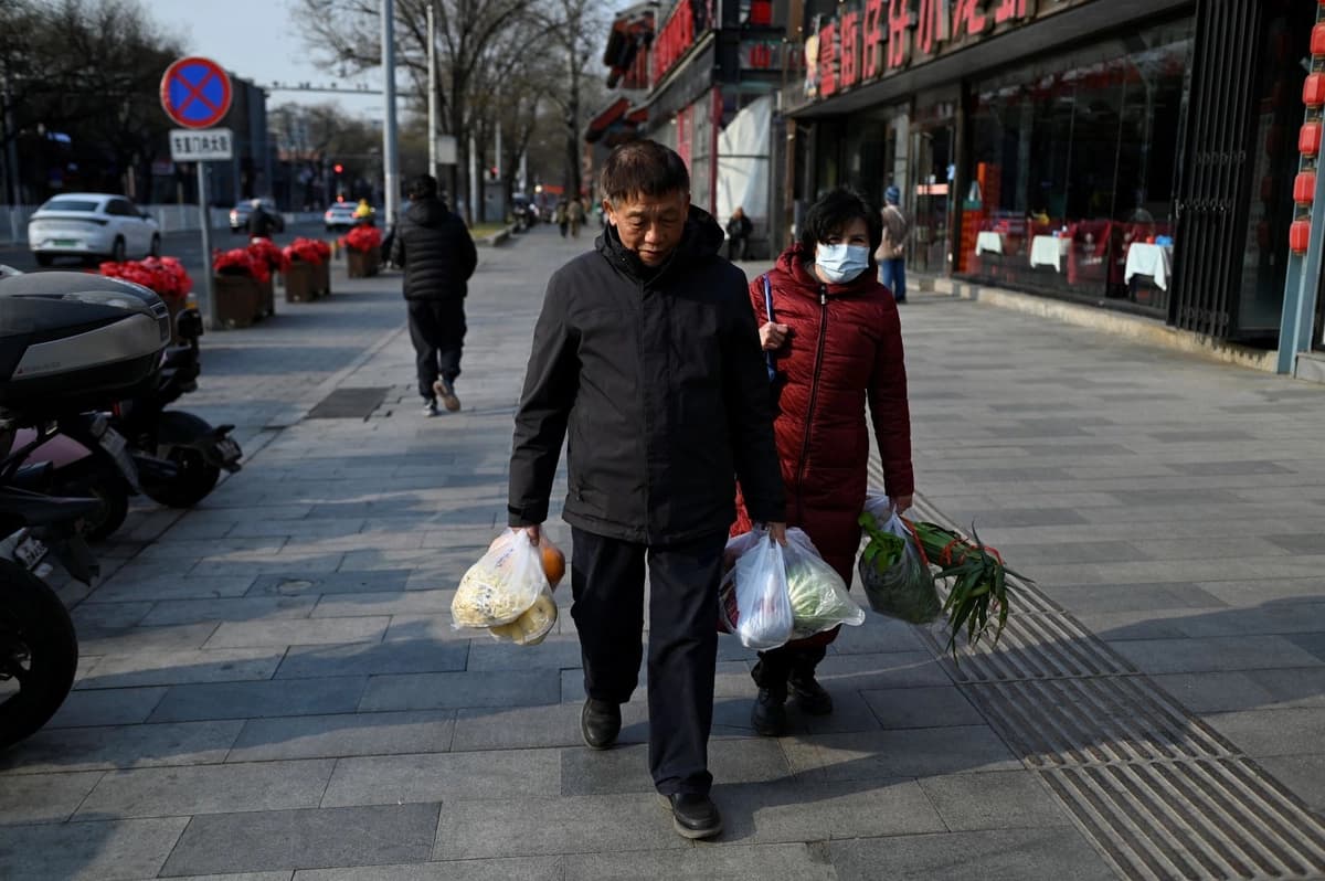<em>Un hombre y una mujer de edad avanzada caminan con sus compras de vegetales frente a un restaurante en Beijing, China, el 22 de diciembre de 2025. (Wang Zhao/AFP vía Getty Images)</em>