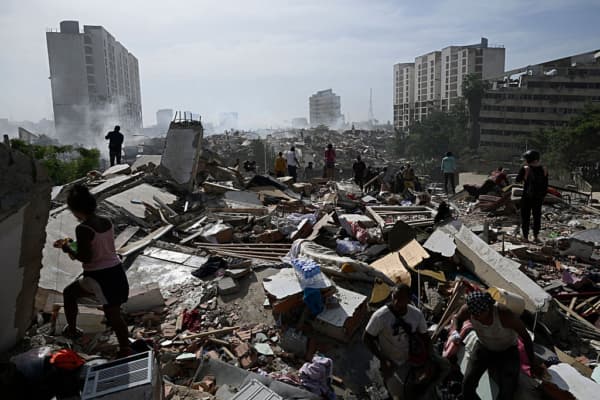 <em>Vecinos caminan entre los escombros tras el doble terremoto en Caraballeda, estado La Guaira, a unos 40 km al noreste de Caracas, el 25 de junio de 2026. Mientras los residentes continúan buscando a sus familiares desaparecidos, las autoridades informaron víctimas mortales y numerosos heridos tras los dos sismos. (Federico PARRA / AFP vía Getty Images)</em>