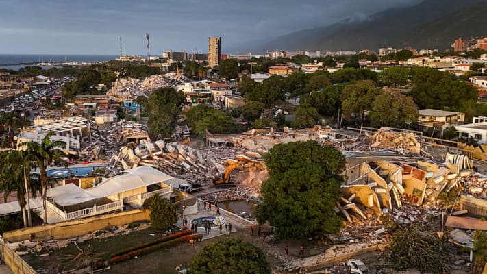 <em>Vista aérea que muestra edificios destruidos tras los dos terremotos en Caraballeda, estado La Guaira, Venezuela, el 29 de junio de 2026. Voluntarios y brigadas de emergencia con perros de rescate continúan removiendo montañas de escombros en busca de sobrevivientes del doble terremoto que golpeó a Venezuela cuatro días antes, derrumbando por completo cerca de 200 edificios y dejando al menos 1450 muertos y decenas de miles de desaparecidos. (Miguel MEDINA / POOL / AFP vía Getty Images)</em>