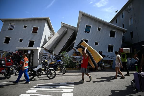 <em>Un hombre carga un colchón frente a edificios residenciales dañados tras un terremoto en Catia La Mar, estado La Guaira, al noroeste de Caracas, el 25 de junio de 2026. El doble terremoto, el mayor registrado en Venezuela en más de un siglo, destruyó edificios cerca de la capital, mientras los residentes buscaban a sus familiares desaparecidos. (Federico PARRA / AFP vía Getty Images)</em>