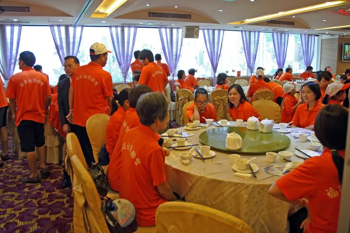 Manifestantes con camisetas que llevan impreso en la espalda "Federación de Asociaciones de Fujian de Hong Kong" disfrutan de una comida en un restaurante como incentivo por haber participado en la reciente marcha antidemocrática en Hong Kong el 17 de agosto de 2014. (Grupos pro-PCCh reservaron todo un restaurante cantonés para ofrecer banquetes a los participantes. The Epoch Times)