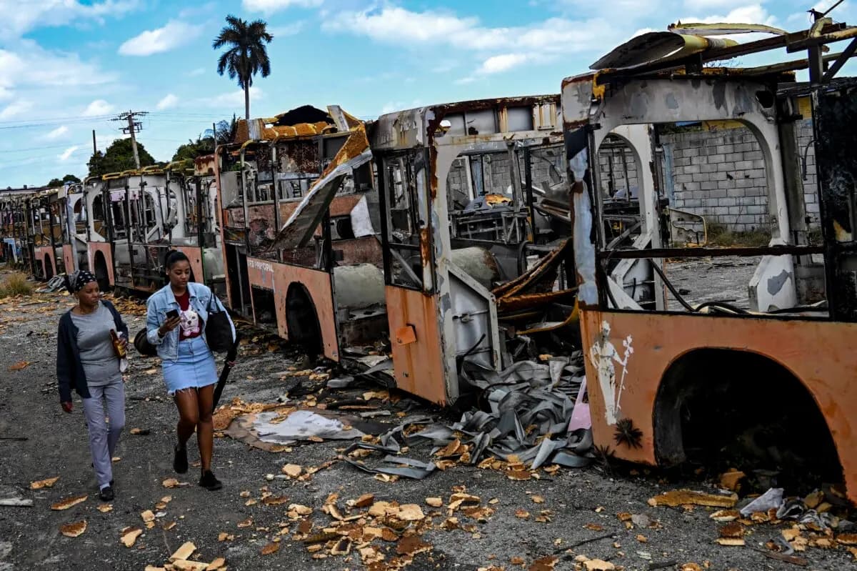 Unas mujeres pasan junto a los restos de autobuses desmantelados y abandonados estacionados en un patio de un barrio del oeste de La Habana, el 5 de julio de 2026. (Yamil Lage/AFP vía Getty Images).