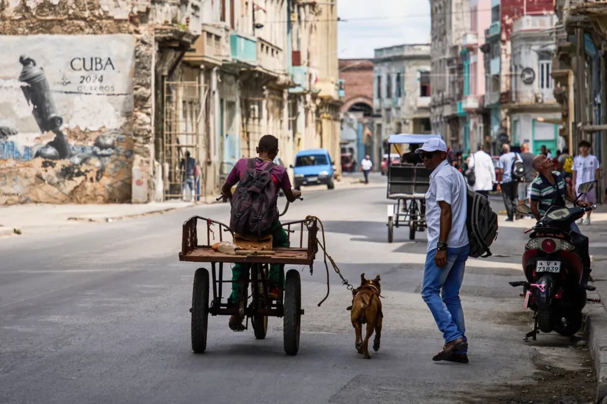 Un hombre anda en triciclo mientras su perro, atado con una correa, corre a su lado durante un apagón en La Habana, Cuba, el 16 de marzo de 2026. (Ramón Espinosa/AP).