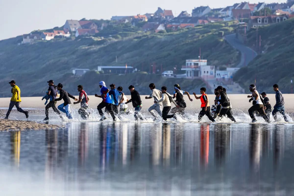 <em>Migrantes se apresuran a abordar una embarcación de traficantes para cruzar el Canal de la Mancha en la playa de Equihen, Francia, el 30 de junio de 2025. (Sameer Al-Doumy/AFP vía Getty Images).</em>