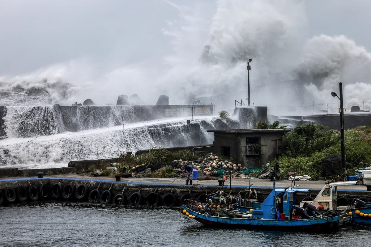 Un pescador maneja una cuerda cerca de un barco pesquero mientras las olas rompen contra un rompeolas a medida que el tifón Bavi avanza hacia el noreste de Taiwán, en Yilan, Taiwán, el 10 de julio de 2026. (I-Hwa Cheng / AFP vía Getty Images)