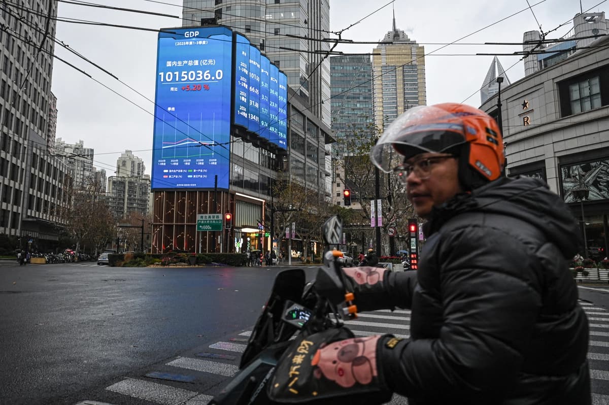 Un hombre pasa en scooter junto a una pantalla que muestra las cifras del producto interior bruto (PIB) en una calle de Shanghái el 19 de enero de 2026. (Jade Gao/AFP vía Getty Images)