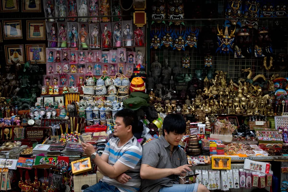 <em>Vendedores consultan sus teléfonos inteligentes mientras esperan clientes en su tienda de souvenirs de fabricación china en el distrito comercial de Wangfujing en Beijing, el 21 de mayo de 2015. (Andy Wong/AP).</em>