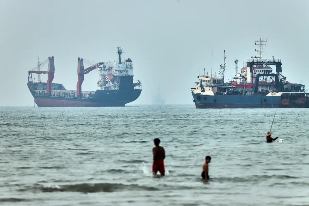 Personas vadean el agua con buques de carga anclados al fondo, en el Estrecho de Ormuz frente a Bandar Abbas, Irán, el 30 de junio de 2026. (Amirhosein Khorgooi/ISNA vía AP)