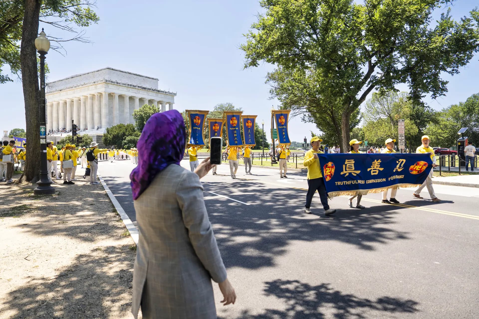 Un transeúnte graba videos de los practicantes de Falun Dafa en Washington el 23 de julio de 2026. (Madalina Kilroy/The Epoch Times)