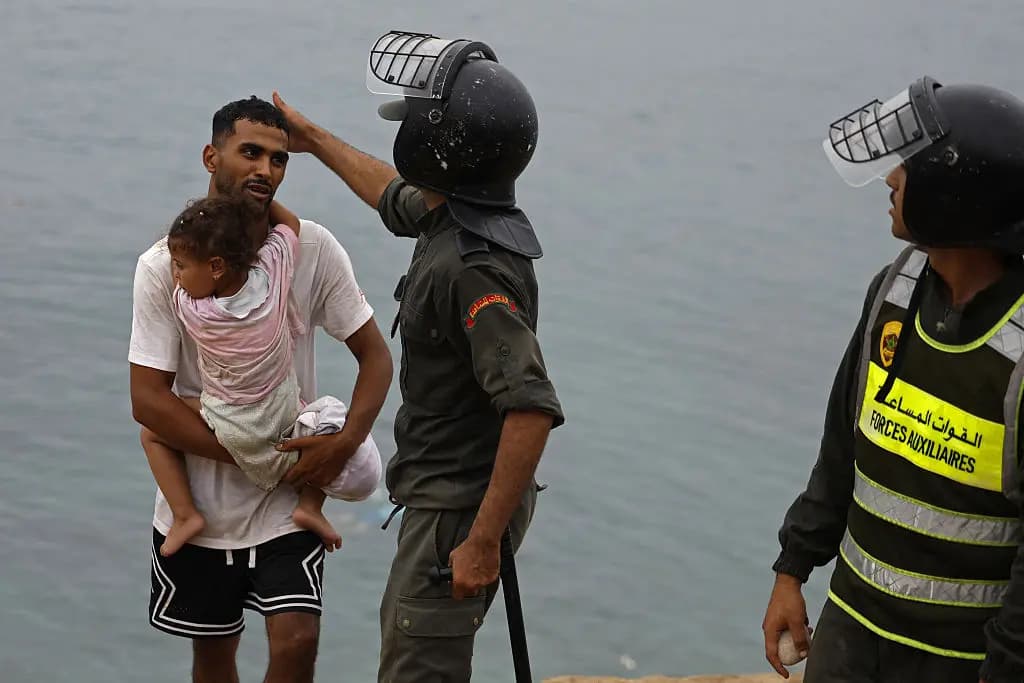 Un miembro de las fuerzas de seguridad marroquíes hace un gesto a un hombre que lleva a un niño cerca del lugar de los enfrentamientos cerca de Fnideq, en la frontera entre Marruecos y España, el 31 de julio de 2026. (Abdel Majid Bziouat/AFP vía Getty Images)