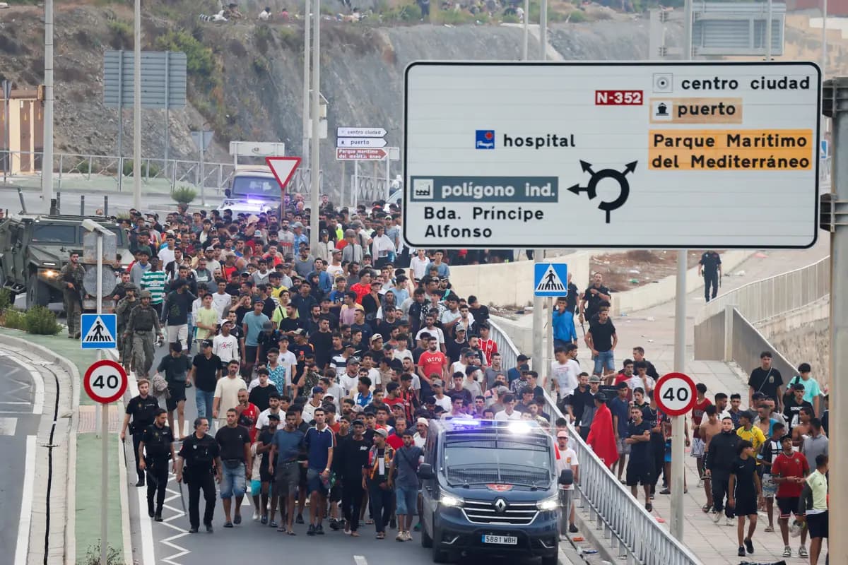 Agentes de policía y soldados españoles escoltan a un numeroso grupo de inmigrantes ilegales hasta la frontera para sacarlos de España, tras los cruces masivos de migrantes a pie y por mar desde Marruecos hacia territorio español, en Ceuta, España, el 1 de agosto de 2026. (Jon Nazca/Reuters).