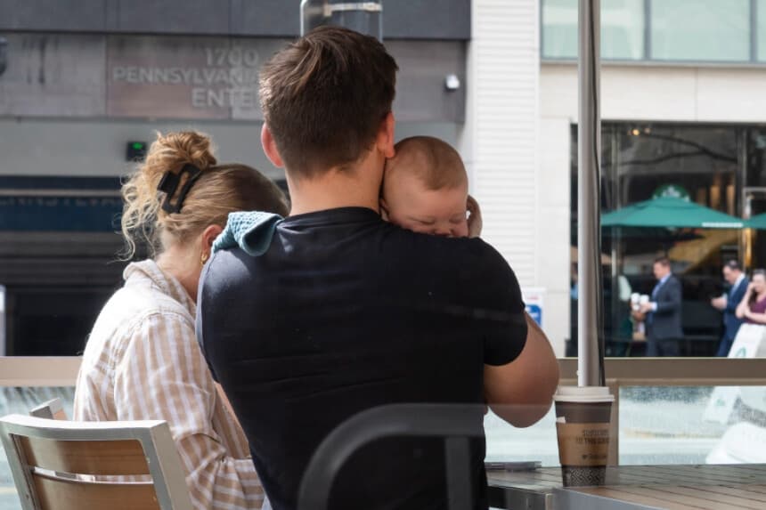 Un hombre sostiene a un bebé frente a una cafetería en Washington el 11 de marzo de 2026. (Madalina Kilroy/The Epoch Times).