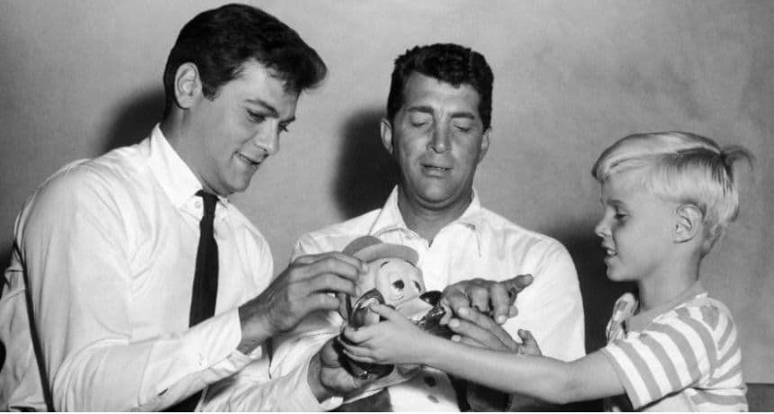 Jay North, joven estrella de la nueva serie "Daniel el Travieso", a la derecha, intenta esposar a Dean Martin, al centro, mientras juegan con un peluche con Tony Curtis, el 15 de septiembre de 1959. (Foto AP, Archivo)