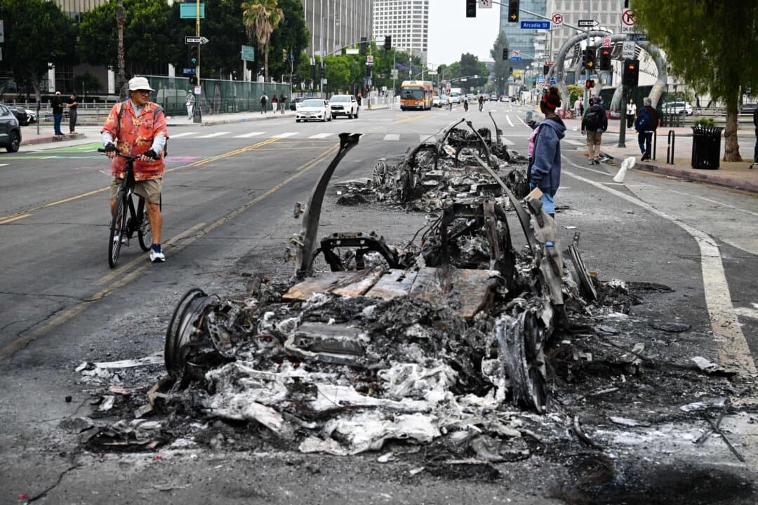 La gente observa los restos carbonizados de un vehículo quemado en la calle tras una noche de protestas en respuesta a las operaciones federales de inmigración en Los Ángeles, el 9 de junio de 2025. (Ronaldo Schemidt/AFP vía Getty Images).