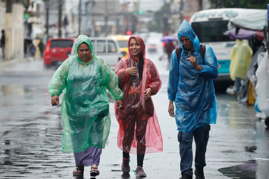 Foto de archivo de tres personas se protegen de la lluvia con capas plásticas en el centro de San Salvador (EFE/Rodrigo Sura)