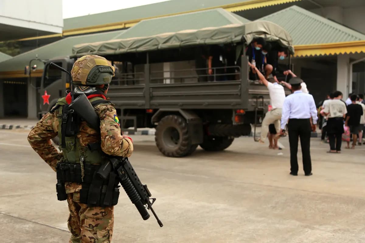 Un miembro del Ejército Nacional Karen, anteriormente Fuerza de Guardia Fronteriza Karen, monta guardia junto a presuntos trabajadores de centros de estafa y víctimas de China que llegan al puesto fronterizo con Tailandia en el municipio oriental de Myawaddy, Birmania, el 20 de febrero de 2025. (STR/AFP vía Getty Images)