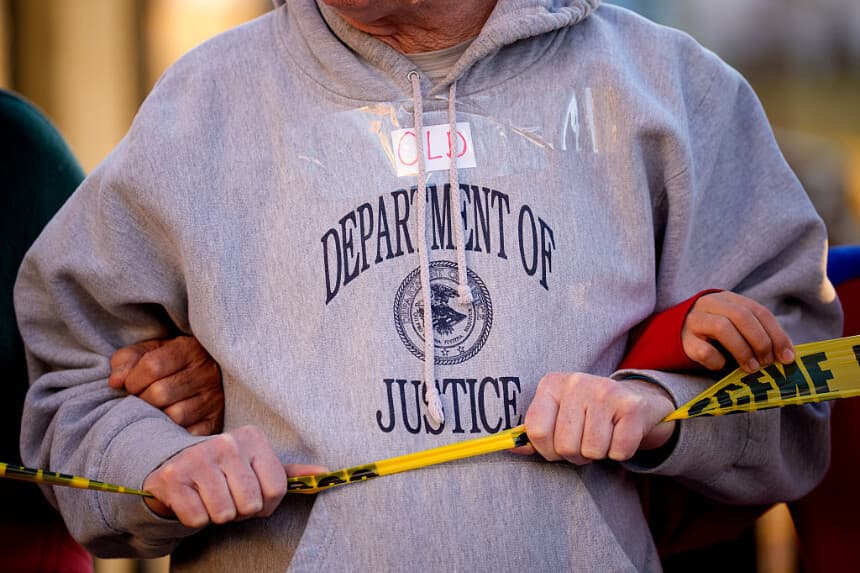 Un hombre pega la palabra "Viejo" en su sudadera del "Departamento de Justicia" y sostienen cinta amarilla de la policía cerca de la Casa Blanca el 24 de noviembre de 2025 en Washington, DC. (Andrew Harnik/Getty Images)