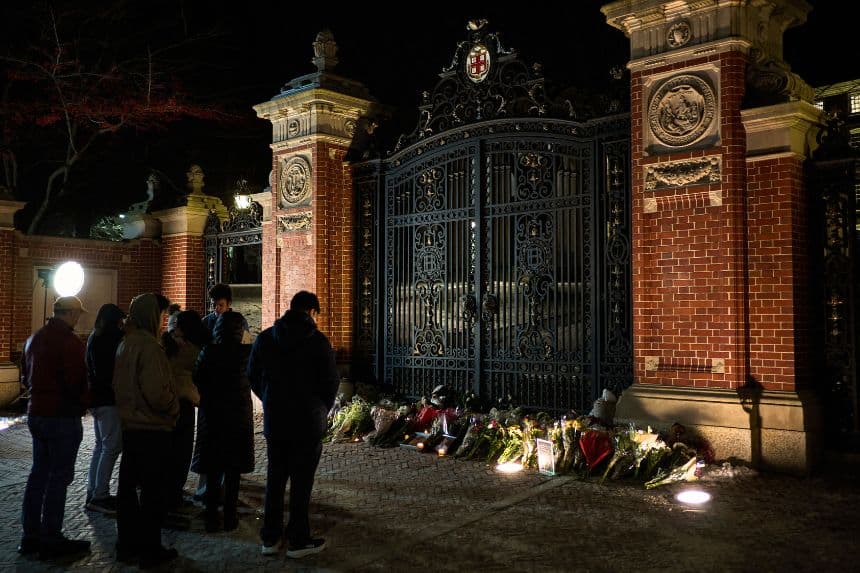 Estudiantes de la Universidad Brown y miembros de la comunidad se detienen un momento ante un memorial improvisado en memoria de las víctimas del tiroteo masivo del 13 de diciembre en las puertas Van Winkle, a las afueras del campus universitario de Brown en Providence, Rhode Island, el 15 de diciembre de 2025.(Bing Guan / AFP a través de Getty Images)