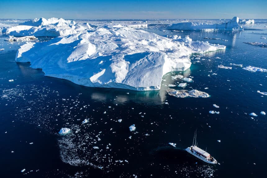 TOPSHOT - Imagen tomada el 30 de junio de 2022 con un dron que muestra un barco con turistas maniobrando entre los icebergs que flotan en la bahía de Disko, Ilulissat, al oeste de Groenlandia. Los icebergs proceden del glaciar Jakobshavn (Sermeq Kujalleq), el glaciar más productivo del hemisferio norte. Los enormes icebergs que se desprenden del glaciar flotan durante años en las aguas frente al fiordo antes de ser arrastrados hacia el sur por las corrientes oceánicas. (Foto de Odd ANDERSEN / AFP) (Foto de ODD ANDERSEN/AFP a través de Getty Images).