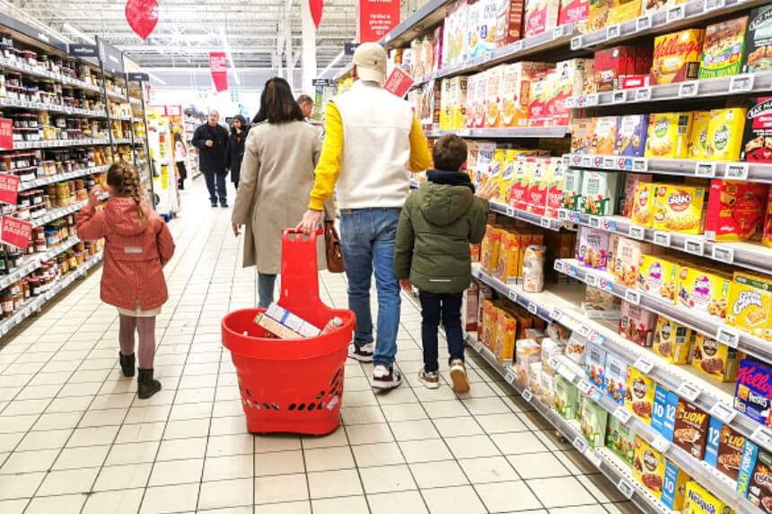 Dos padres y sus dos hijos caminan por una sección de pasteles, galletas y mermeladas, con el padre tirando de una cesta llena de artículos, en el supermercado Auchan de Guilherand Granges, Francia, el 1 de febrero de 2025. (Nicolas Guyonnet / Hans Lucas/AFP vía Getty Images).