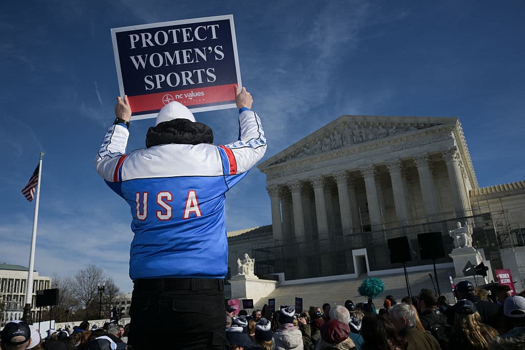 Un hombre sostiene un cartel con el lema "Proteger los deportes femeninos" mientras se manifiesta frente a la Corte Suprema de Estados Unidos, mientras los jueces escuchan los argumentos en los recursos contra las prohibiciones estatales a los atletas transgénero en los deportes femeninos, el 13 de enero de 2026, en Washington D. C. (Foto de Oliver Contreras / AFP a través de Getty Images)