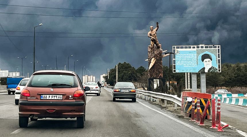 Vehículos circulan por una autopista junto a una estatua conmemorativa de guerra y una valla publicitaria que representa al difunto líder supremo de Irán, el ayatolá Ali Khamenei, quien murió en un ataque aéreo el 28 de febrero, mientras se alzaban columnas de humo negro, en Teherán, el 8 de marzo de 2026. (AFP vía Getty Images)