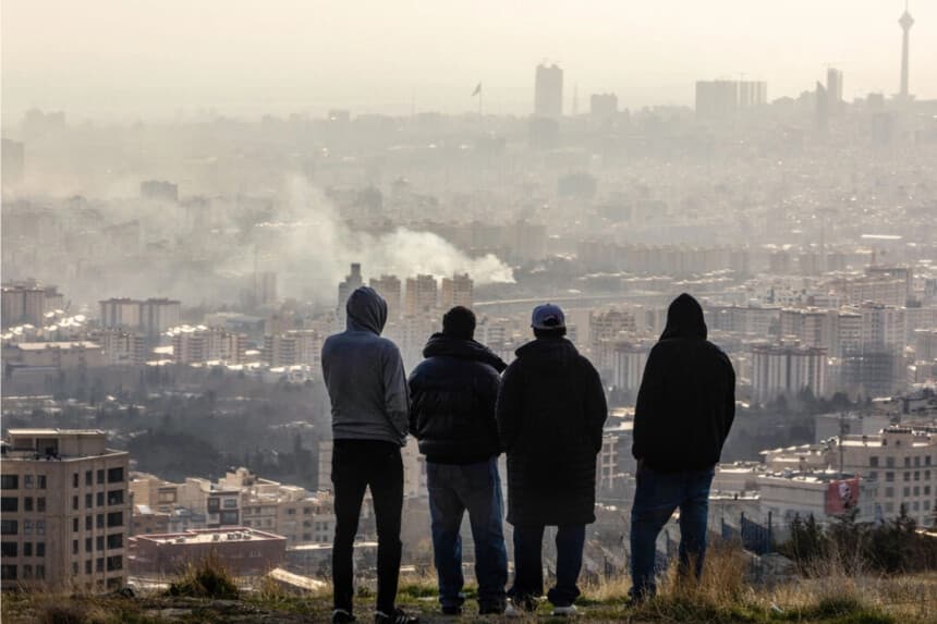 Los hombres observan desde una ladera cómo se eleva una columna de humo después de una explosión en Teherán, Irán, el 2 de marzo de 2026. (Majid Saeedi/Getty Images)