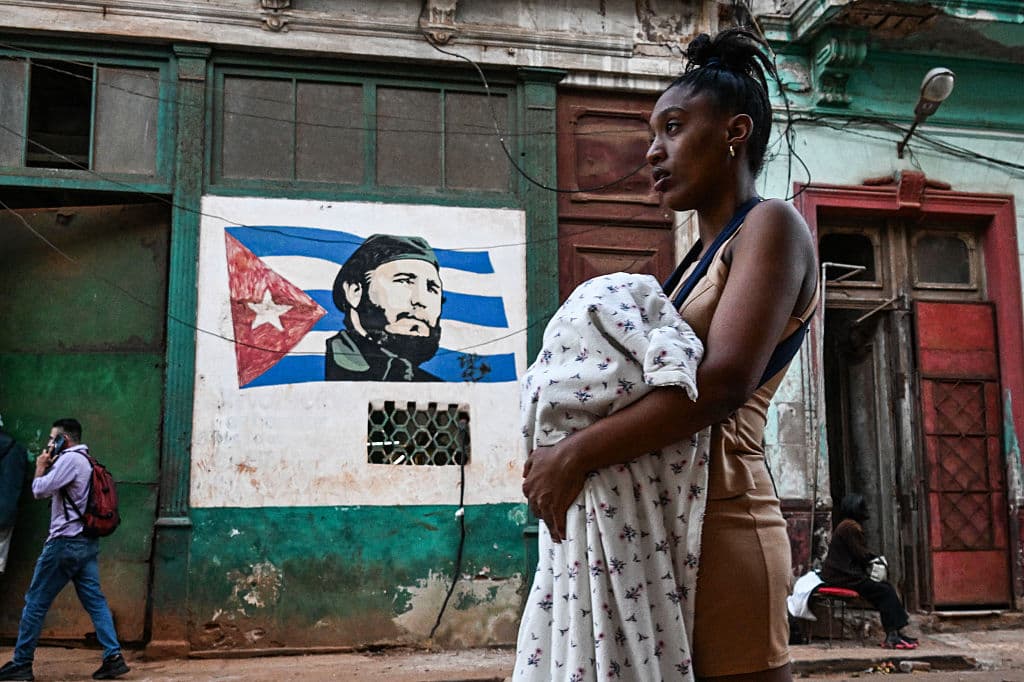 Una mujer camina frente a una imagen de la bandera cubana y del fallecido presidente cubano Fidel Castro durante un apagón en La Habana el 4 de marzo de 2026. (Foto de YAMIL LAGE / AFP vía Getty Images)