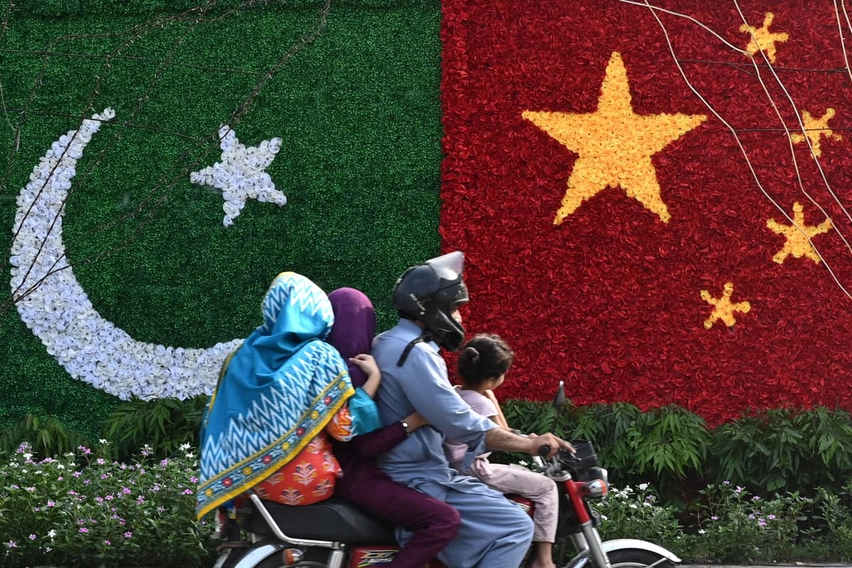 Una familia pasa en bicicleta junto a una decoración con la forma de las banderas nacionales de China y Pakistán, instalada a lo largo de una carretera antes de la visita del viceprimer ministro chino He Lifeng, en Lahore, el 30 de julio de 2023. (Arif Ali/AFP vía Getty Images)