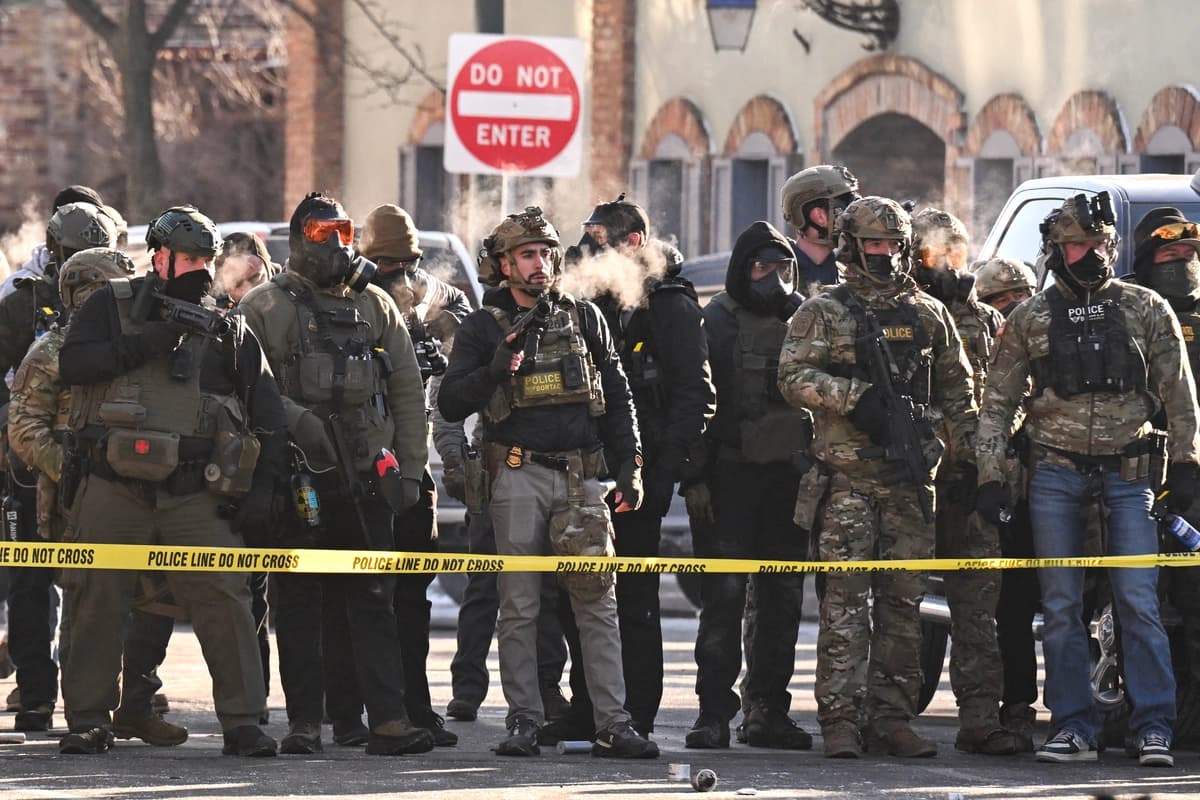 Agentes federales permanecen tras la cinta policial mientras manifestantes se congregan cerca del lugar donde, según las autoridades estatales y locales, un hombre fue baleado por agentes federales en la madrugada del 24 de enero de 2026 en Minneapolis. (Roberto Schmidt/AFP vía Getty Images)