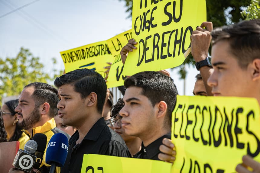 Jóvenes del partido opositor Primero Justicia (PJ) sostienen carteles durante una protesta frente a las oficinas del Concejo Nacional Electoral (CNE), en Maracaibo, Venezuela. (EFE/ Henry Chirinos)