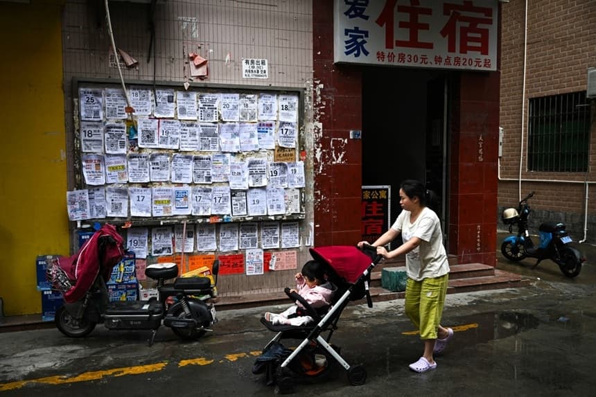 Una mujer empuja un cochecito con un bebé junto a anuncios de empleo exhibidos en un tablero en Foshan, provincia de Guangdong, en China, el 28 de abril de 2026. (Pedro Pardo / AFP vía Getty Images)