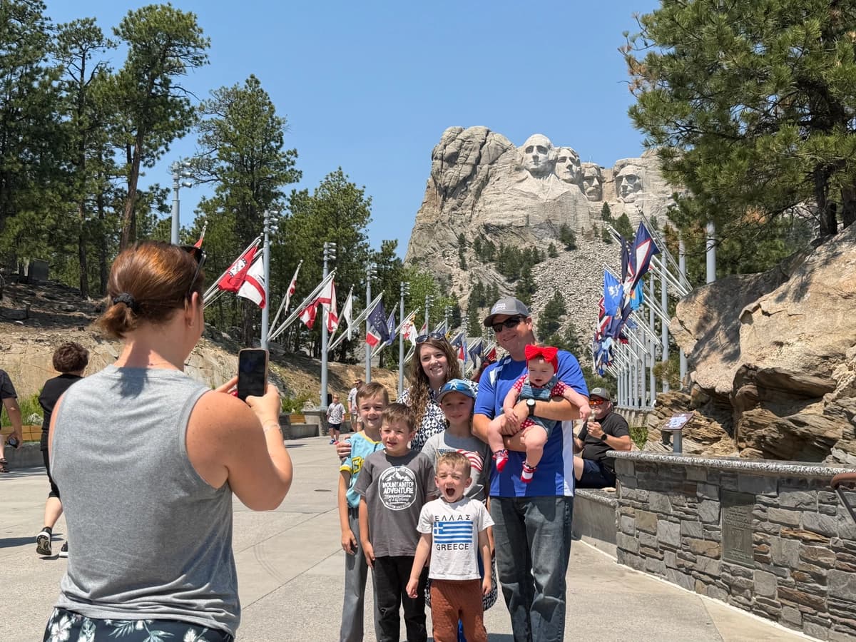 Paul Rains (derecha), quien vive cerca de Milwaukee, Wisconsin, sostiene a su hija y posa con su esposa, Lisa, y sus otros cuatro hijos mientras una mujer les toma una foto en el Monte Rushmore, en Keystone, Dakota del Sur, el 2 de julio de 2026. (Janice Hisle/The Epoch Times)