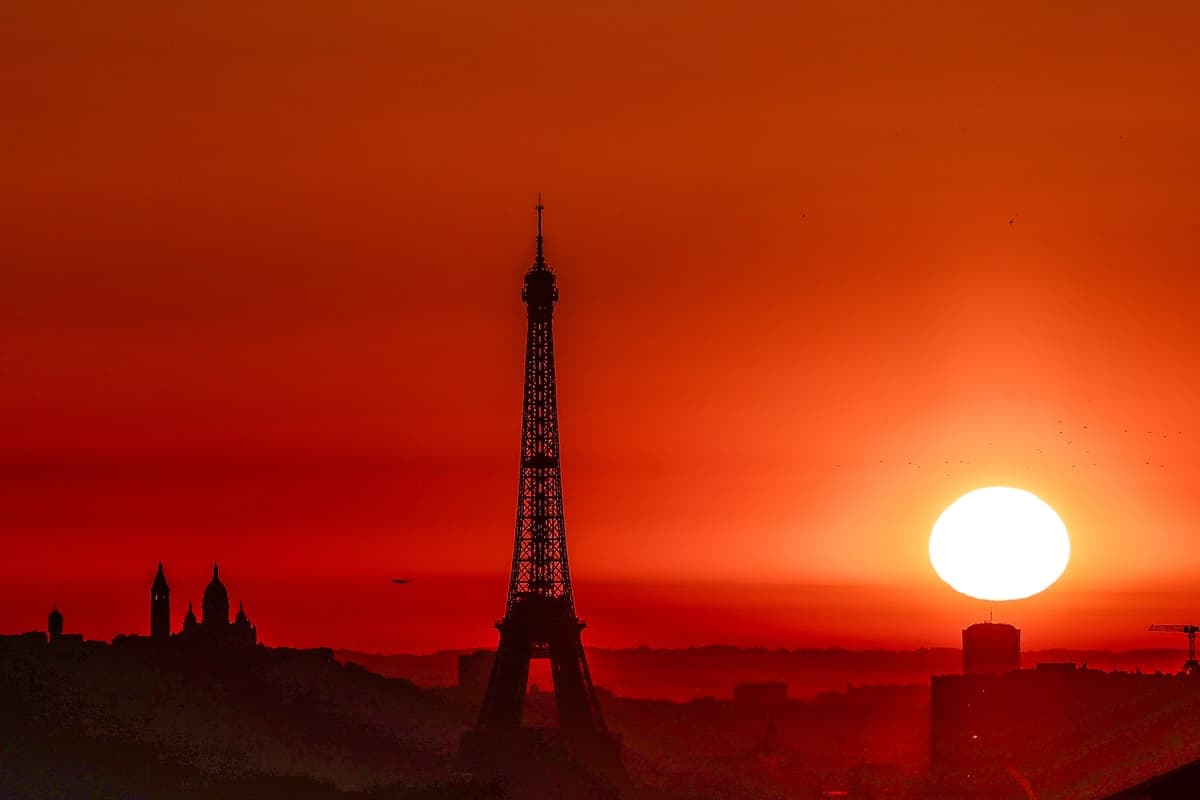 El sol sale con la Torre Eiffel y la Basílica del Sacré-Cœur en la cima de la colina de Montmartre en París el 1 de julio de 2025. (Thibaud Moritz/AFP vía Getty Images).