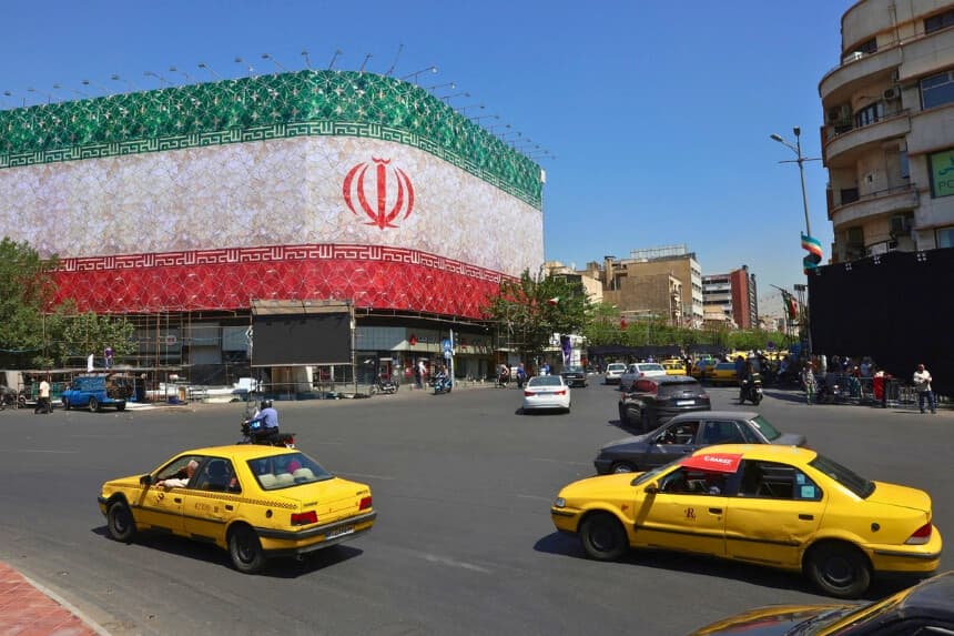 El tráfico pasa junto a la bandera nacional iraní que ondea en un edificio de la plaza Enghelab en Teherán, Irán, el 14 de junio de 2026. (AFP vía Getty Images).
