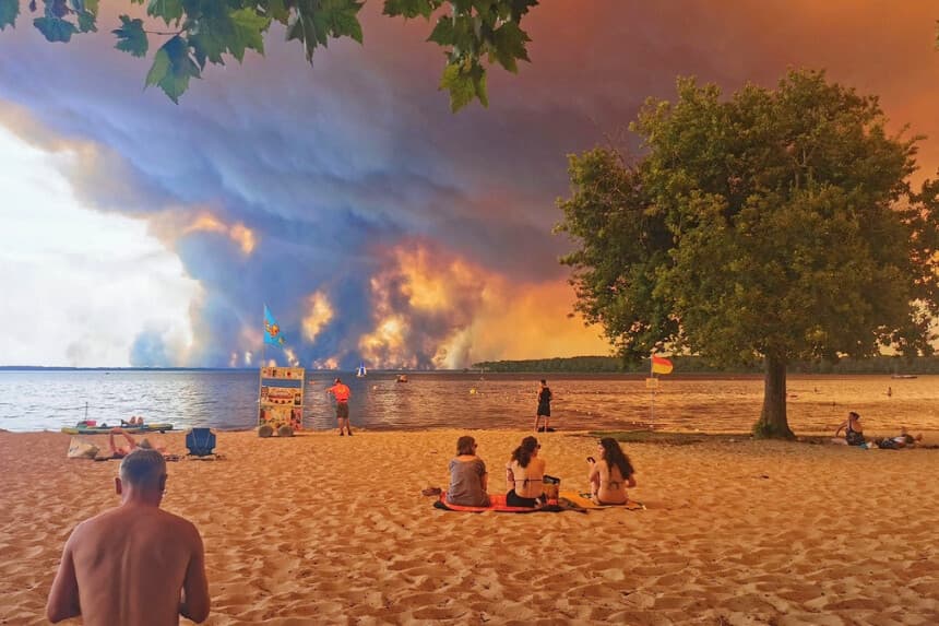 Los banyistas se sientan en la playa de Moutchic mientras nubes de humo se elevan al cielo tras un incendio forestal en Lacanau, Francia, el 24 de julio de 2026. (Maximilien Lamy/AFP vía Getty Images).