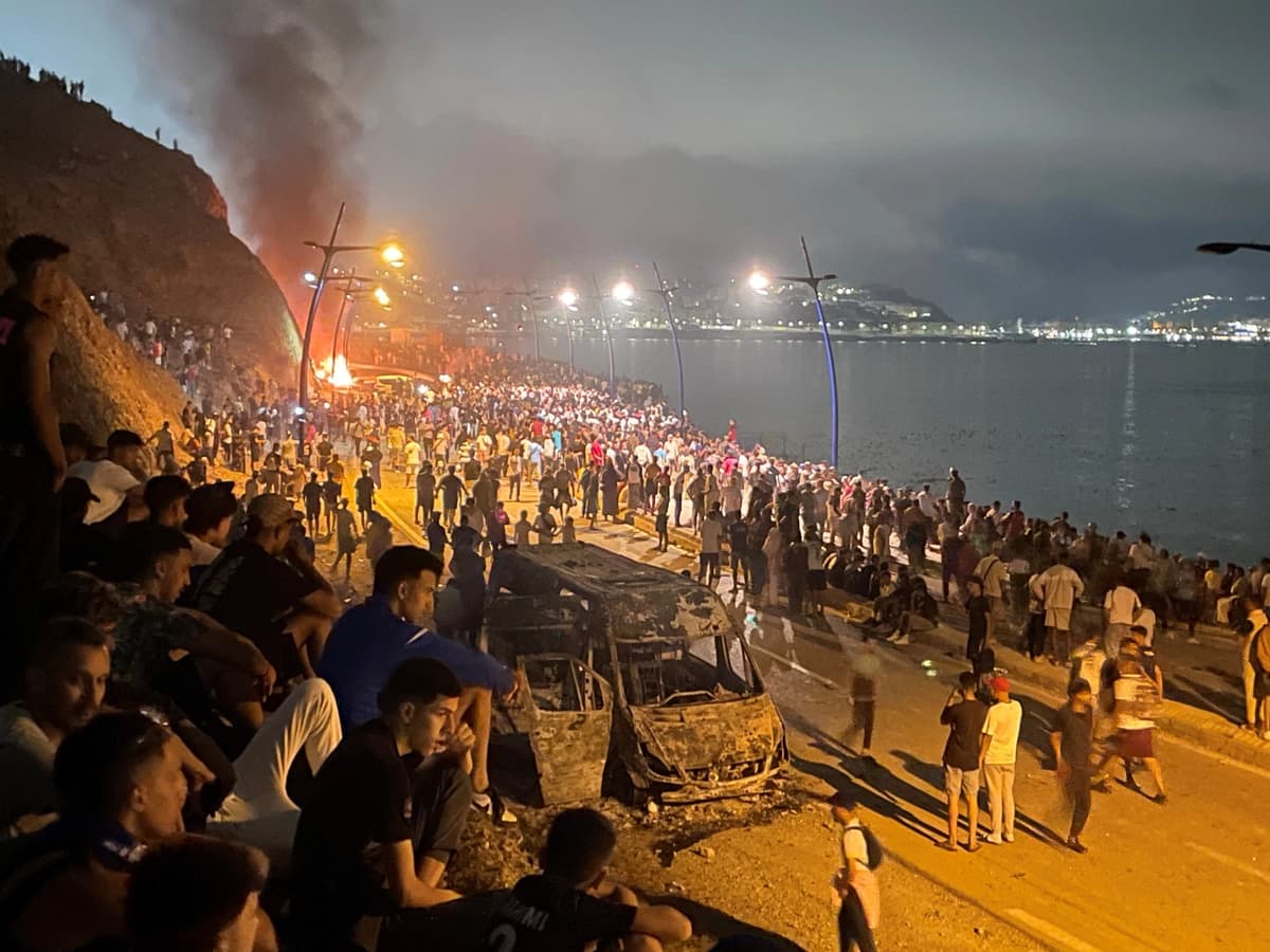 Los migrantes se reúnen alrededor de un vehículo incendiado mientras esperan la oportunidad de cruzar al enclave español de Ceuta, en el lado marroquí de la frontera en Fnideq, Marruecos, el 31 de julio de 2026. (Ahmed El Jechtimi /Reuters)