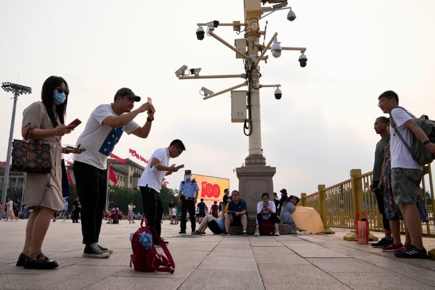 Un policía monta guardia junto a unas cámaras de vigilancia mientras la gente hace fotos en la plaza de Tiananmen, en Beijing, el 15 de julio de 2021. (Ng Han Guan /AP Photo).